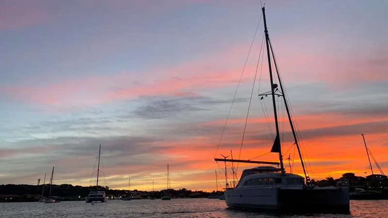 Tortuga Yacht Photos Pics Lagoon 380 catamaran silhouetted against a vibrant sunset sky over calm waters.