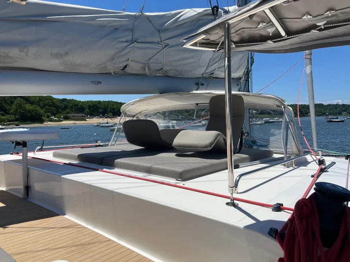 Tri It Yacht Photos Pics Luxurious NEEL 51 trimaran deck with sun loungers, 2018 model, docked by a scenic shoreline.