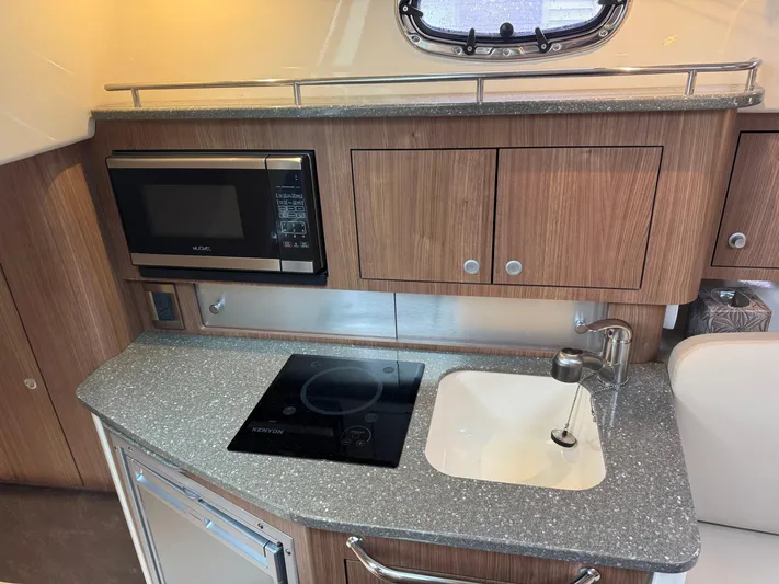  Yacht Photos Pics 2019 Boston Whaler 315 Conquest kitchen with microwave, stove, sink, and wooden cabinetry.