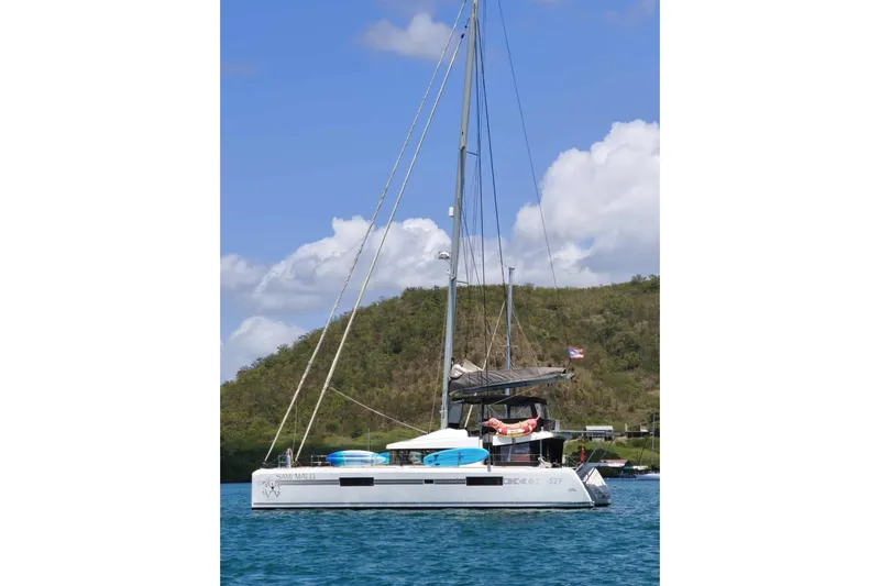 Sami Malu Yacht Photos Pics 2017 Lagoon 52 F catamaran sailing on blue water near a lush green hillside.