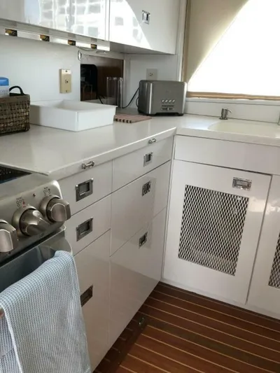 Dovetail Yacht Photos Pics 1972 Trumpy 72 Houseboat kitchen with white cabinets, stainless steel appliances, and wooden flooring.