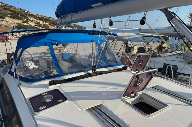 Yacht Photos Pics 2011 Jeanneau 53 sailboat with blue canopy, open hatches, docked by rocky shoreline.