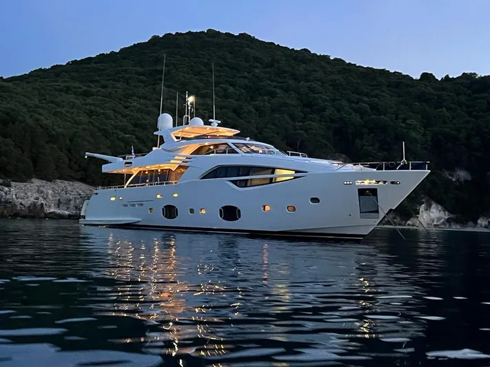  Yacht Photos Pics Luxurious 2012 Custom Line 100 yacht illuminated at dusk, anchored near a forested hillside.