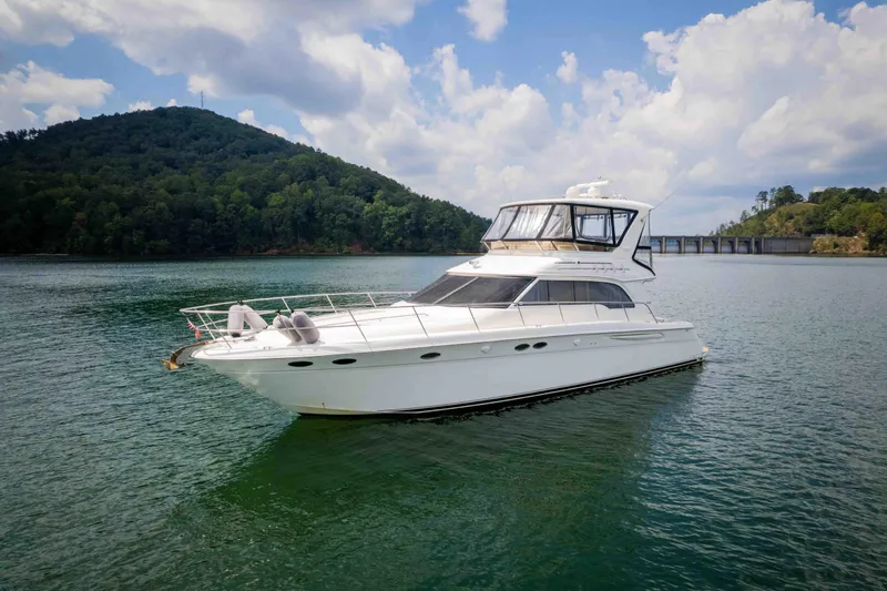  Yacht Photos Pics 1999 Sea Ray 480 Sedan Bridge yacht on a serene lake with lush hills.