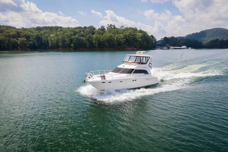  Yacht Photos Pics 1999 Sea Ray 480 Sedan Bridge cruising on a scenic lake under a partly cloudy sky.