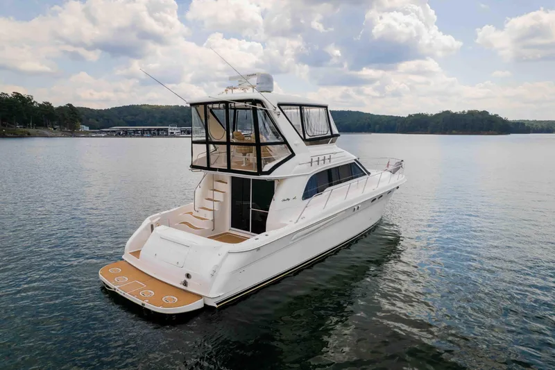  Yacht Photos Pics 1999 Sea Ray 480 Sedan Bridge yacht on a serene lake under a cloudy sky.