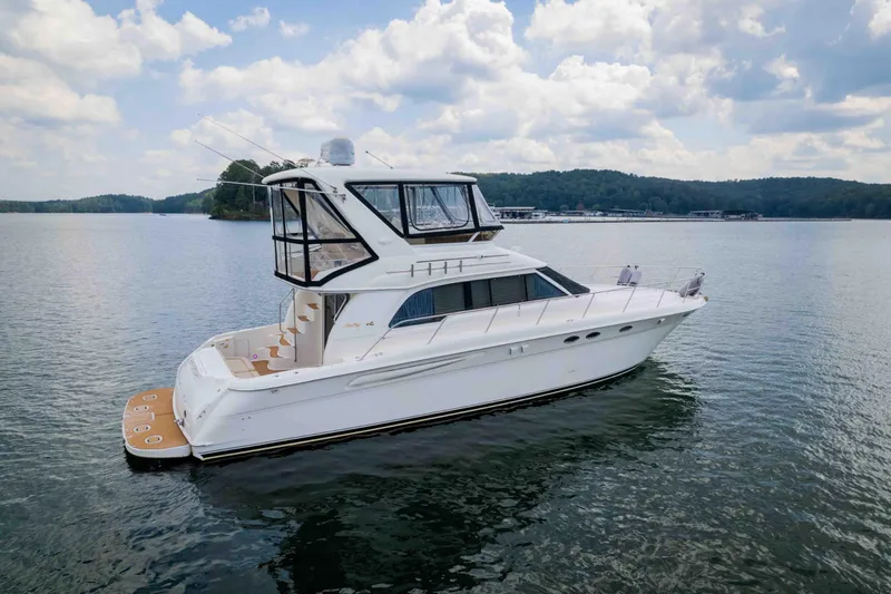  Yacht Photos Pics 1999 Sea Ray 480 Sedan Bridge yacht on a serene lake under a cloudy sky.