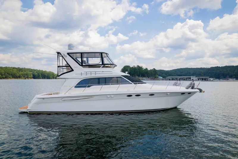  Yacht Photos Pics 1999 Sea Ray 480 Sedan Bridge yacht on a serene lake under a cloudy sky.