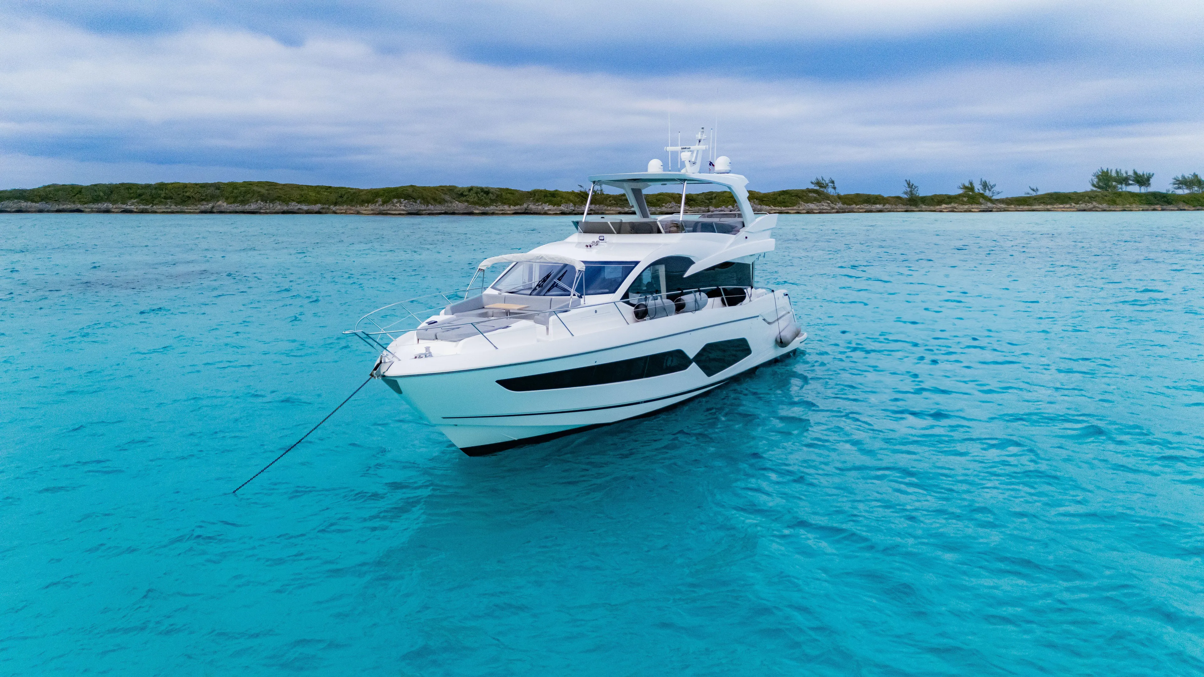 O Legasea Yacht Photos Pics 2018 Sunseeker Manhattan 66 yacht on turquoise water, under a cloudy sky.