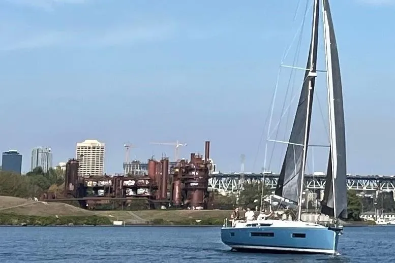 Atticus Yacht Photos Pics 2022 Jeanneau Sun Odyssey 490 sailing near industrial structures and city skyline.