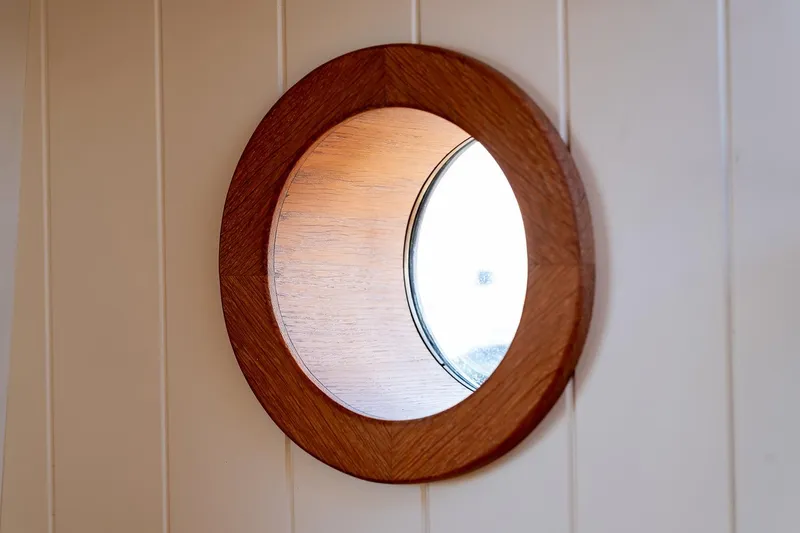 Jaleo Yacht Photos Pics Wooden-framed porthole window on Puffin 50, 2019 model, with light reflection.