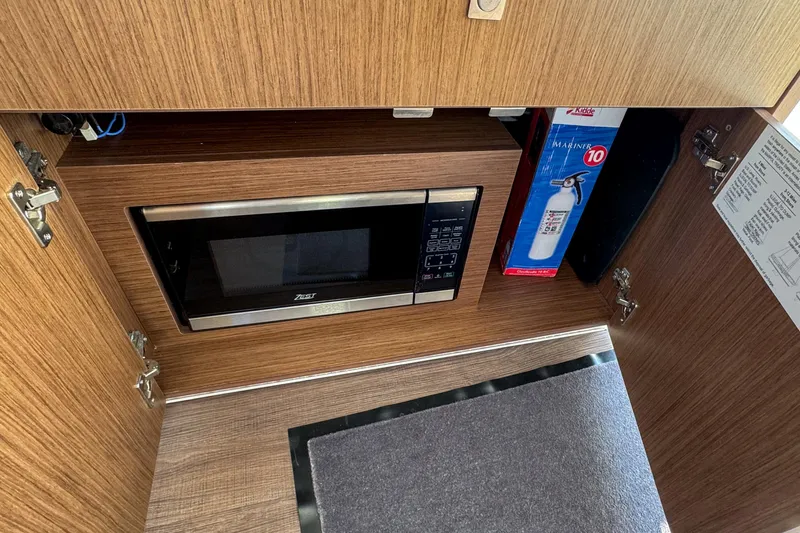  Yacht Photos Pics 2025 Beneteau Antares 9 interior with microwave and fire extinguisher in wooden cabinet.