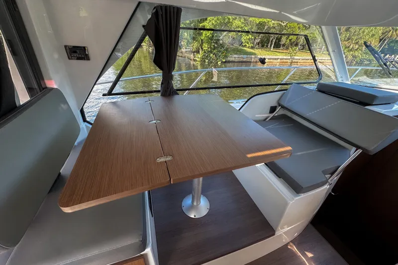  Yacht Photos Pics Interior of 2025 Beneteau Antares 9, featuring a wooden table and seating by a window.