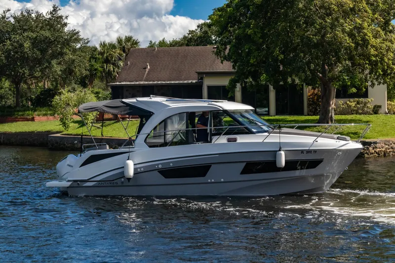  Yacht Photos Pics 2025 Beneteau Antares 9 cruising on a scenic waterway near a house.