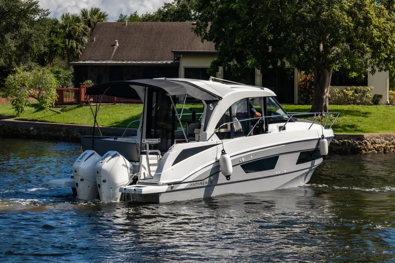  Yacht Photos Pics 2025 Beneteau Antares 9 motorboat cruising on a scenic waterway near a house.