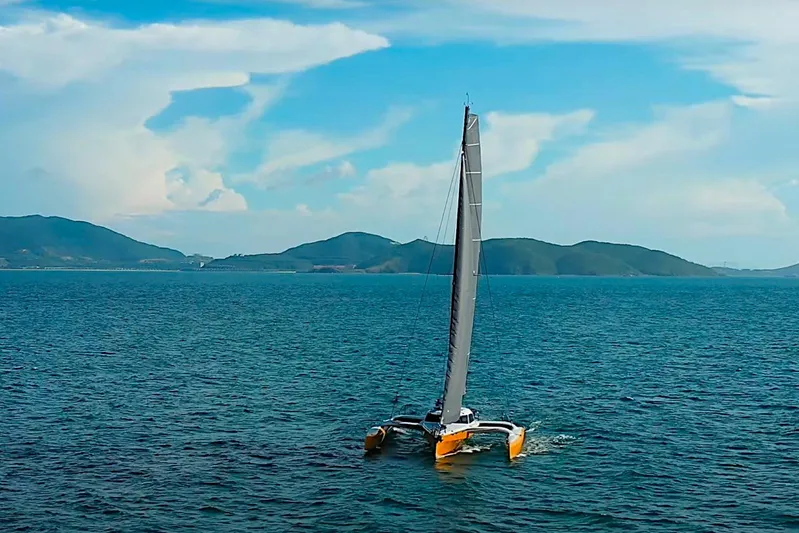  Yacht Photos Pics Sleek 2026 Rapido 60 trimaran sailing on open sea with scenic mountain backdrop.
