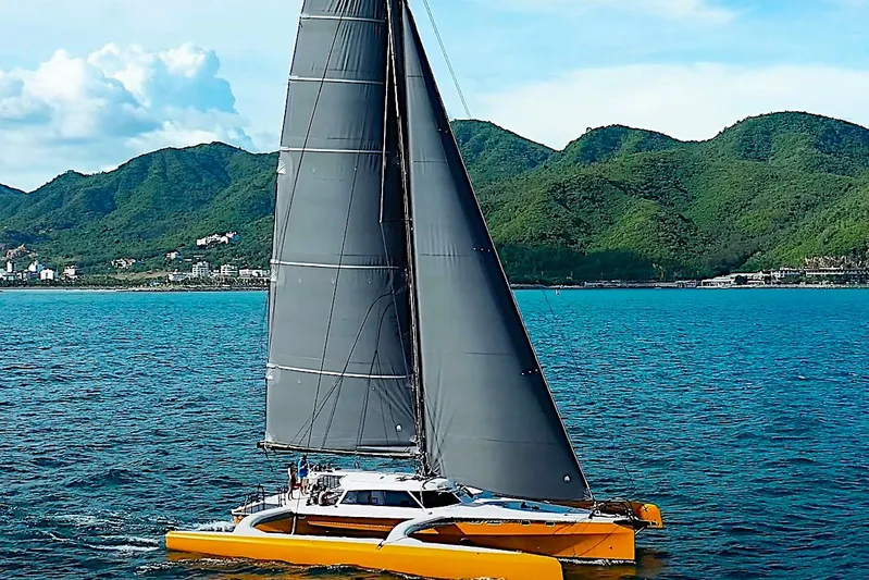  Yacht Photos Pics Sleek 2026 Rapido 60 catamaran sailing on blue ocean with lush green mountains in background.