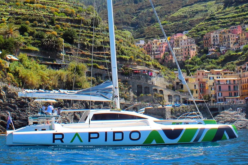  Yacht Photos Pics Rapido 60 trimaran sailing near colorful coastal village, 2026 model.