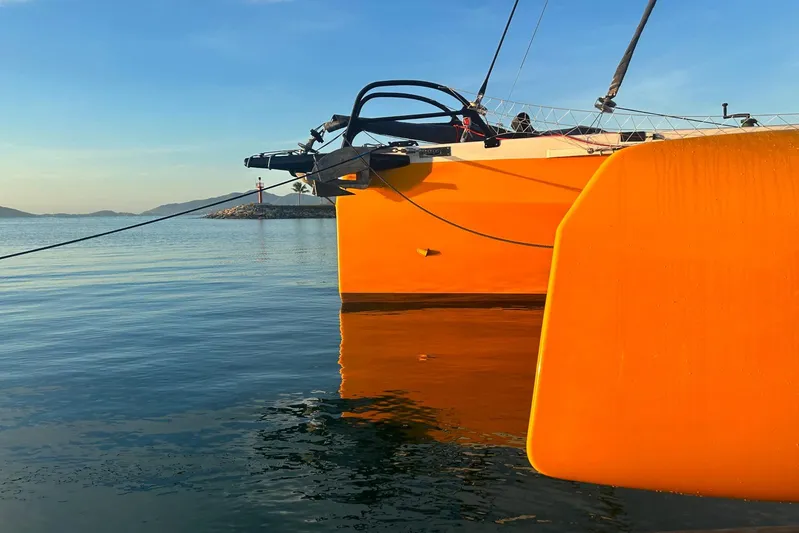  Yacht Photos Pics Orange Rapido 60 trimaran on calm water, 2026 model, with clear blue sky.