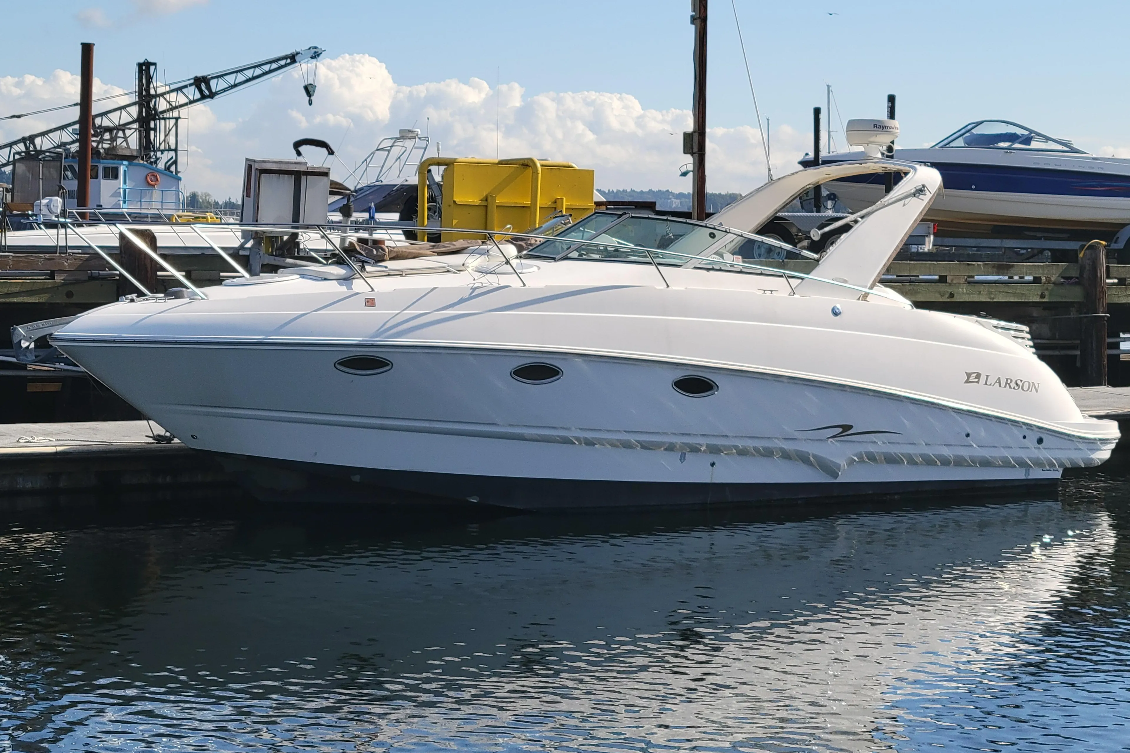 2003 Larson 310 boat docked at a marina, with clear skies and industrial background.
