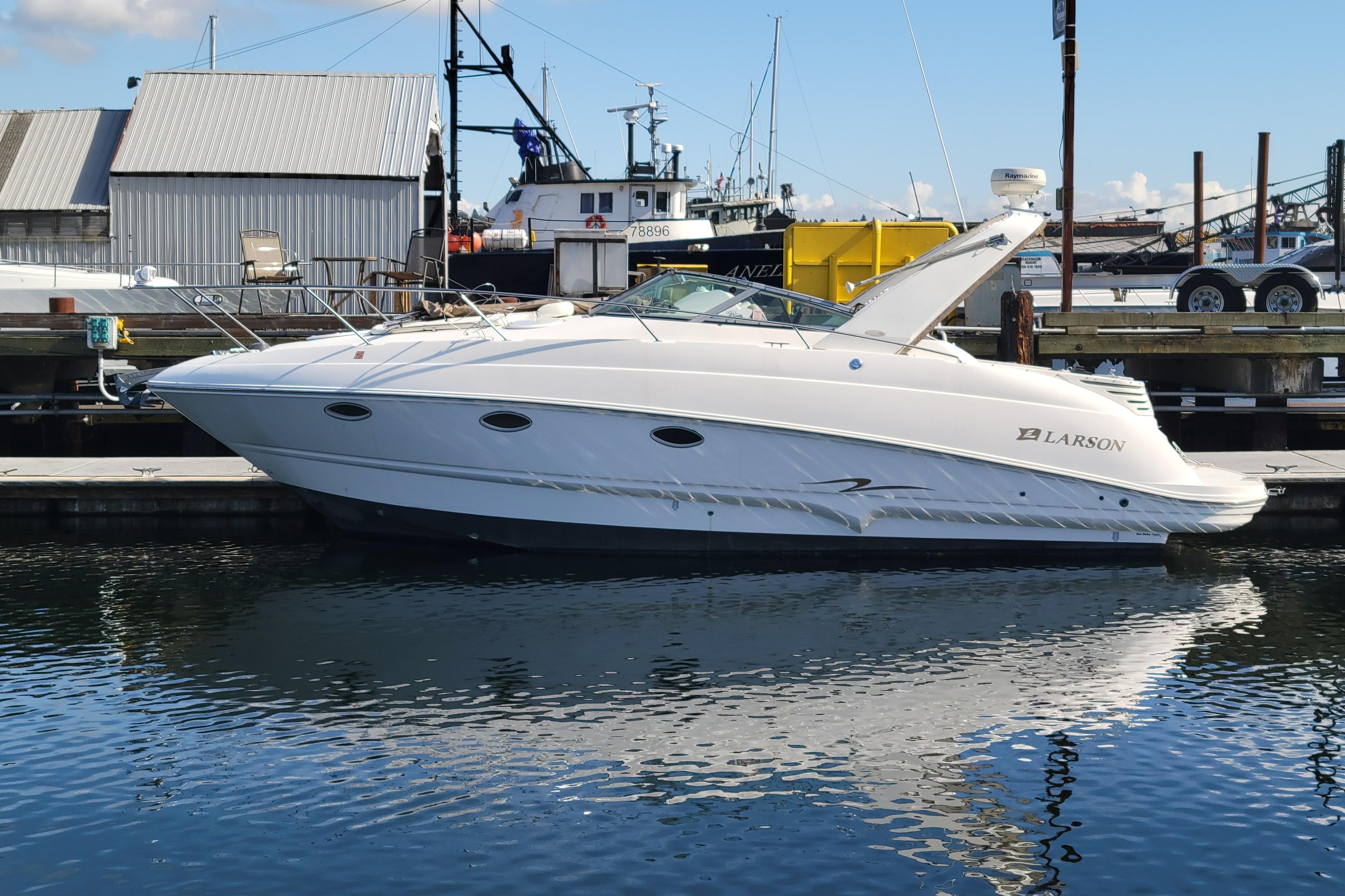 2003 Larson 310 boat docked at marina, reflecting on calm water.