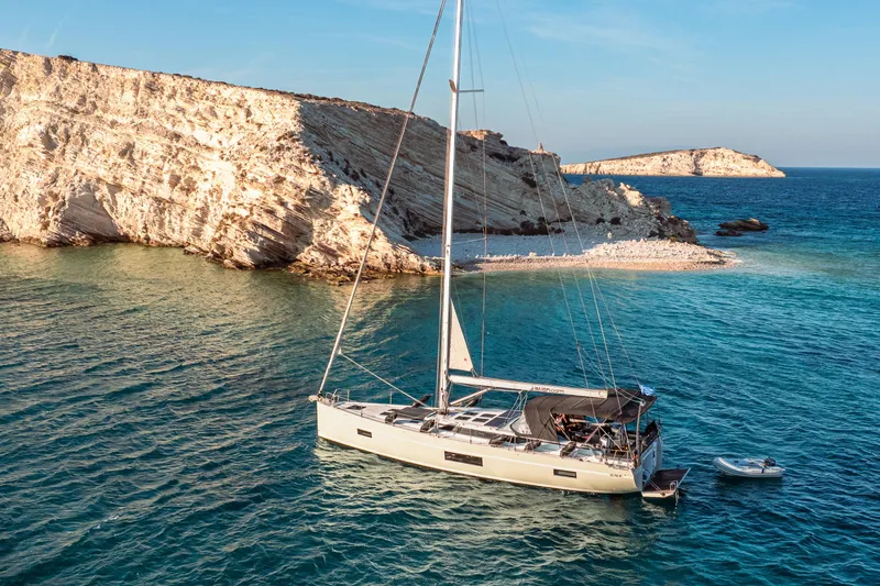  Yacht Photos Pics Sailing yacht Bavaria C57 (2022) anchored near rocky coastline in clear blue waters.