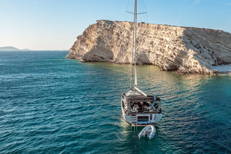  Yacht Photos Pics Sailing yacht Bavaria C57 (2022) anchored near rocky coastline in clear blue waters.