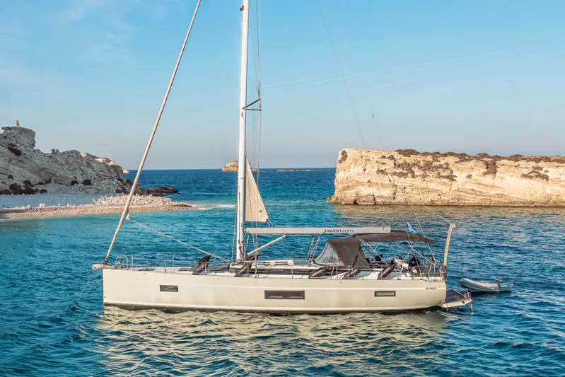 Yacht Photos Pics Sailing yacht Bavaria C57, 2022 model, anchored in clear blue waters near rocky coastline.