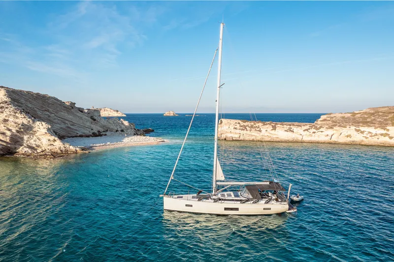  Yacht Photos Pics Sailing yacht Bavaria C57 (2022) anchored in a serene, rocky coastal bay.