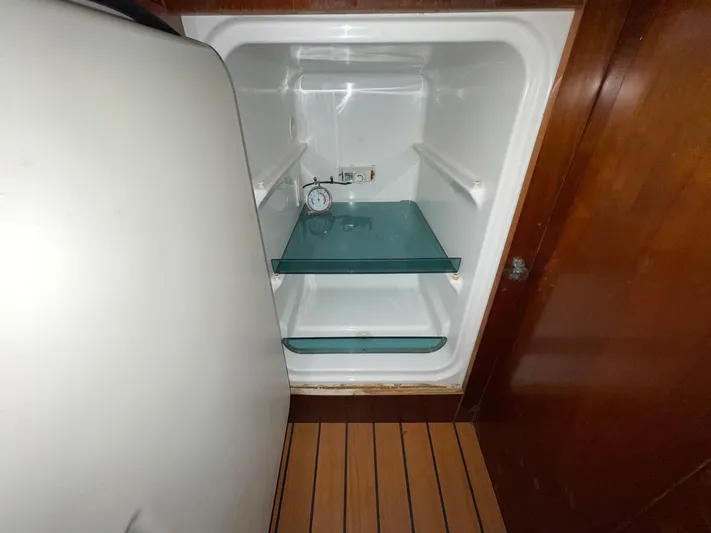Abra Cadabra Yacht Photos Pics Empty refrigerator inside 2004 Beneteau Oceanis 423 yacht, featuring glass shelves and wooden flooring.