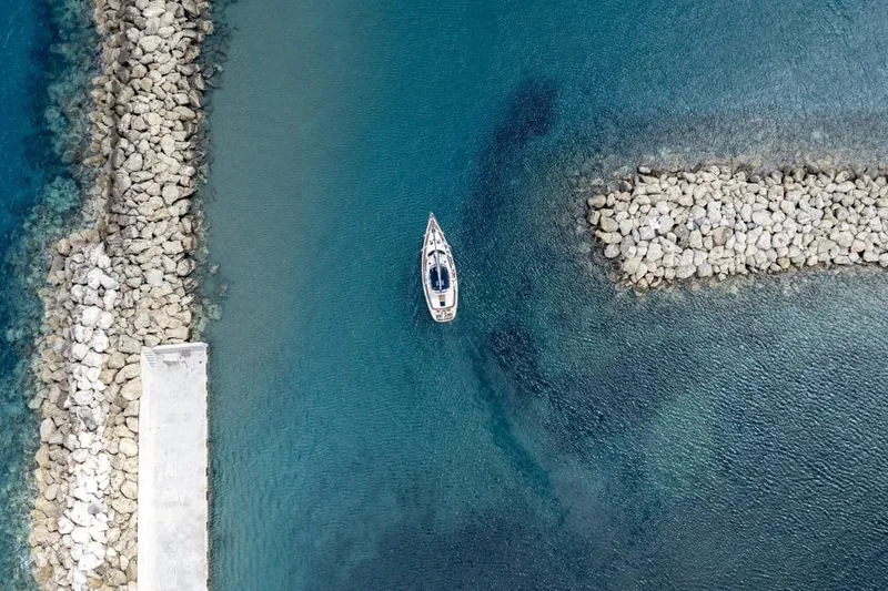 Yacht Photos Pics Aerial view of 2000 Hunter 45 Center Cockpit sailboat in clear blue water near rocky breakwater.