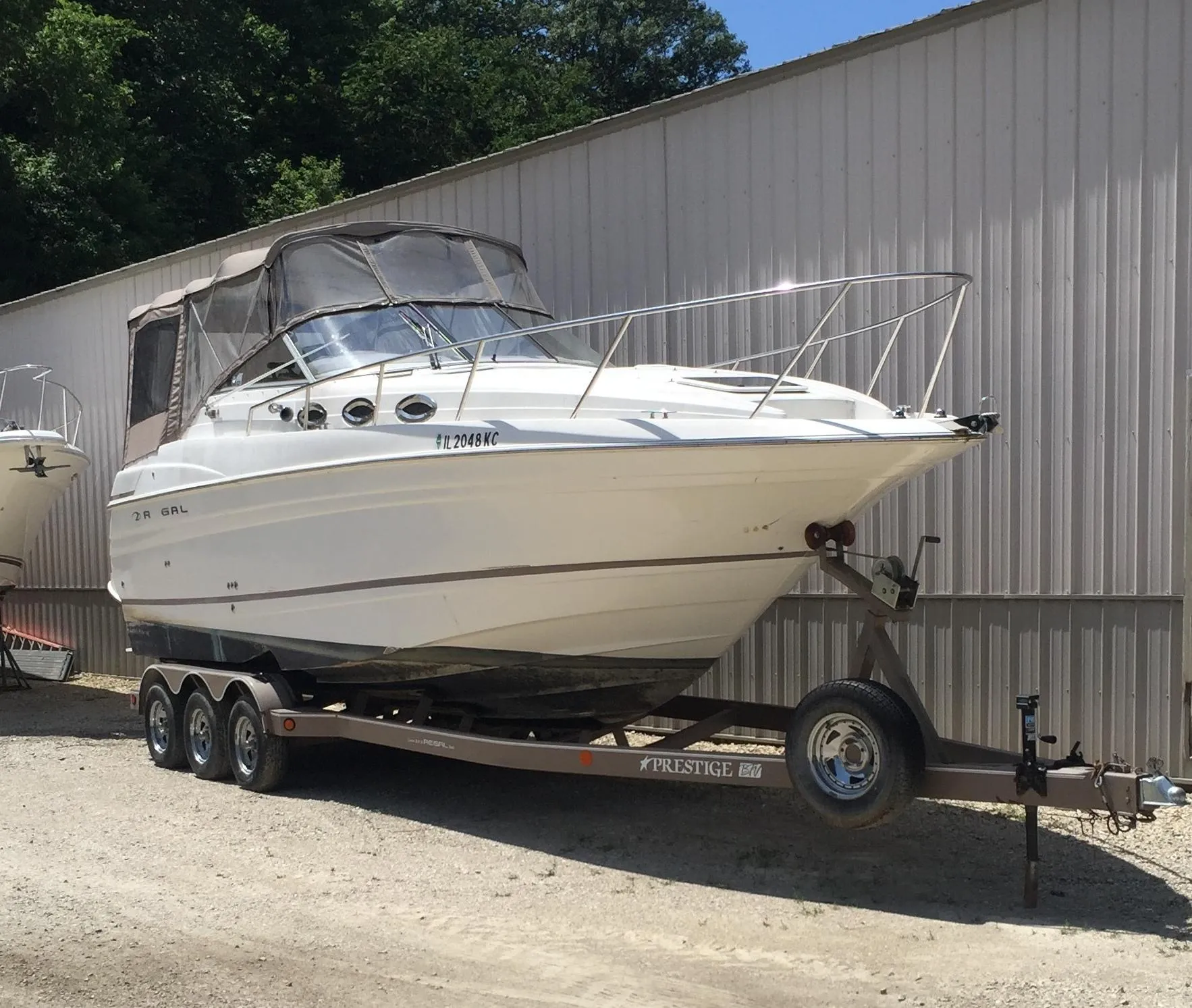 2003 Regal 2765 boat on trailer, parked outdoors near a metal building.