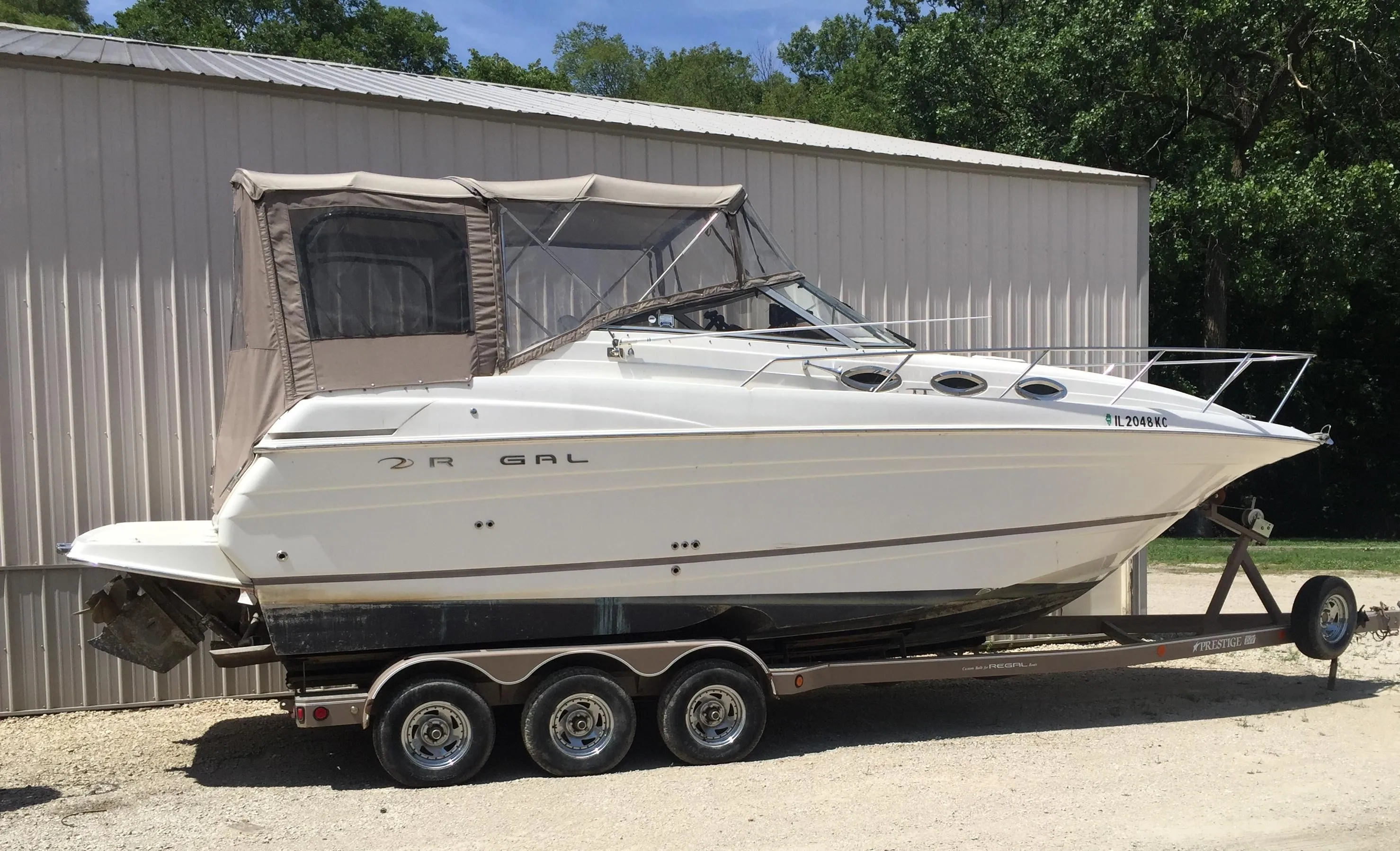 2003 Regal 2765 boat on trailer, parked beside a metal building.