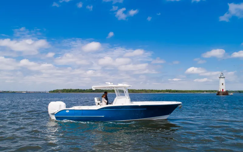  Yacht Photos Pics 2025 Buddy Davis 28 Center Console boat cruising near a lighthouse on a sunny day.