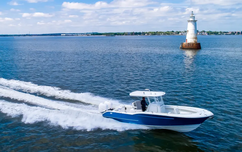  Yacht Photos Pics 2025 Buddy Davis 28 Center Console boat cruising near a lighthouse on a sunny day.