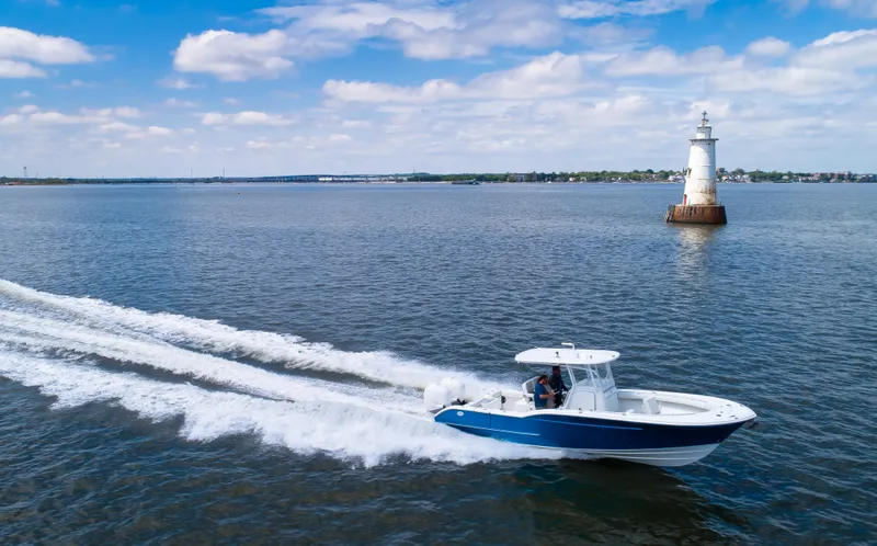  Yacht Photos Pics 2025 Buddy Davis 28 Center Console boat cruising near a lighthouse on a sunny day.