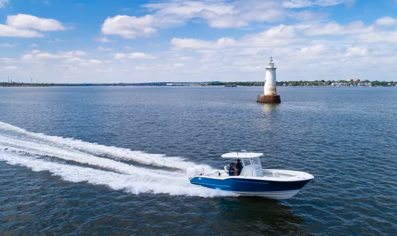  Yacht Photos Pics 2025 Buddy Davis 28 Center Console boat cruising near a lighthouse on a sunny day.