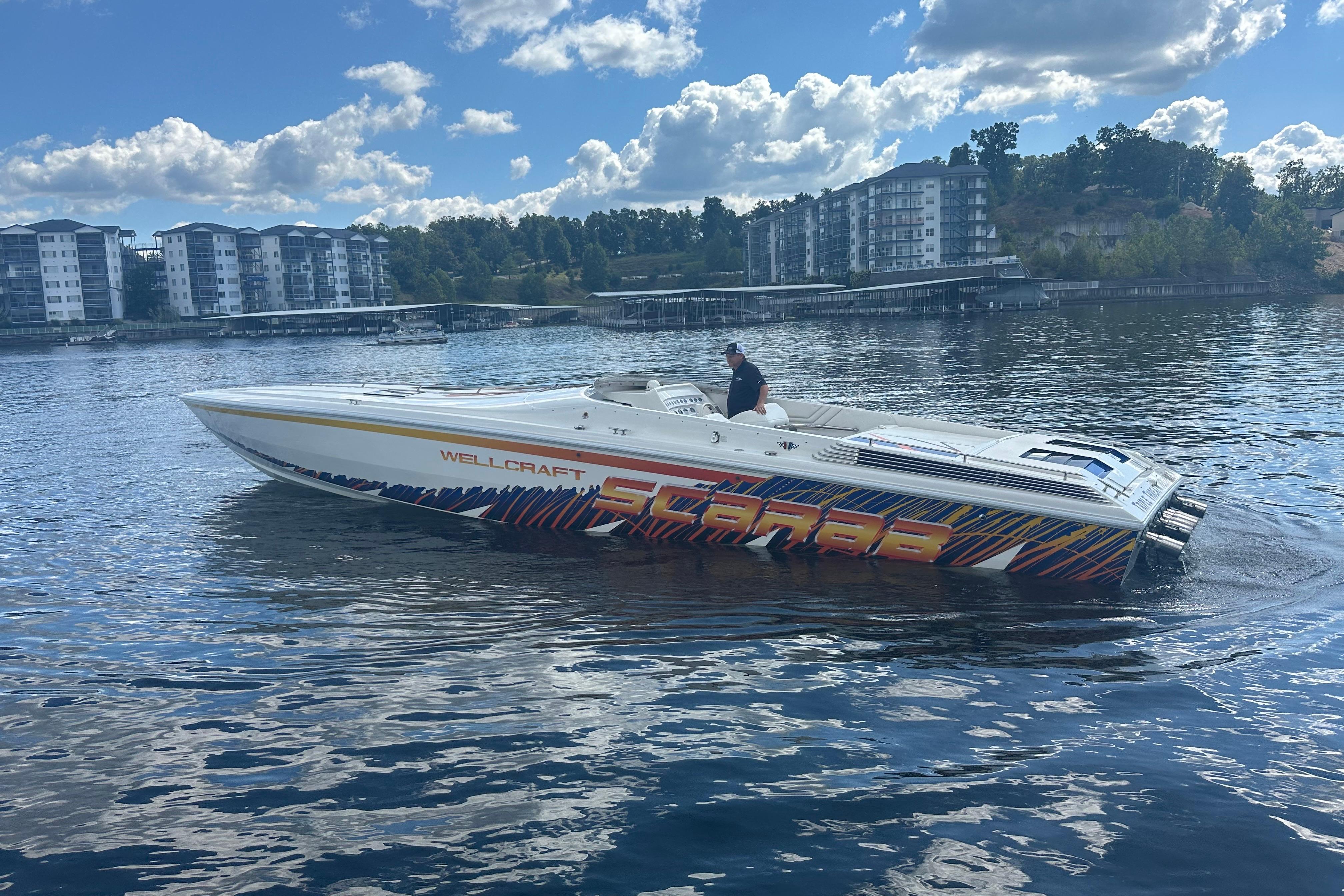 1995 Excel Scarab 43 speedboat on water, with vibrant graphics and modern buildings in background.