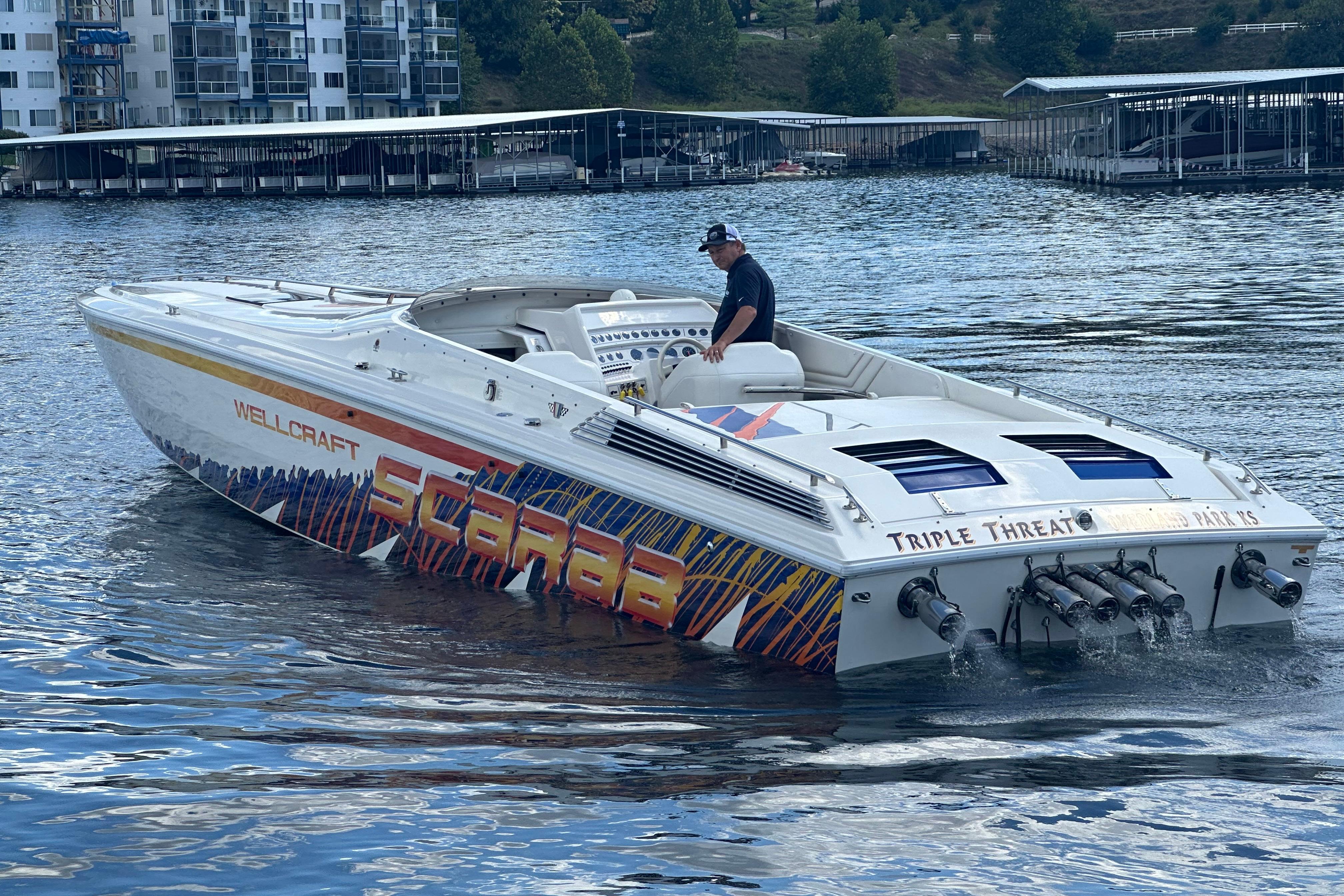 1995 Excel Scarab 43 speedboat on water, vibrant graphics, dock and buildings in background.