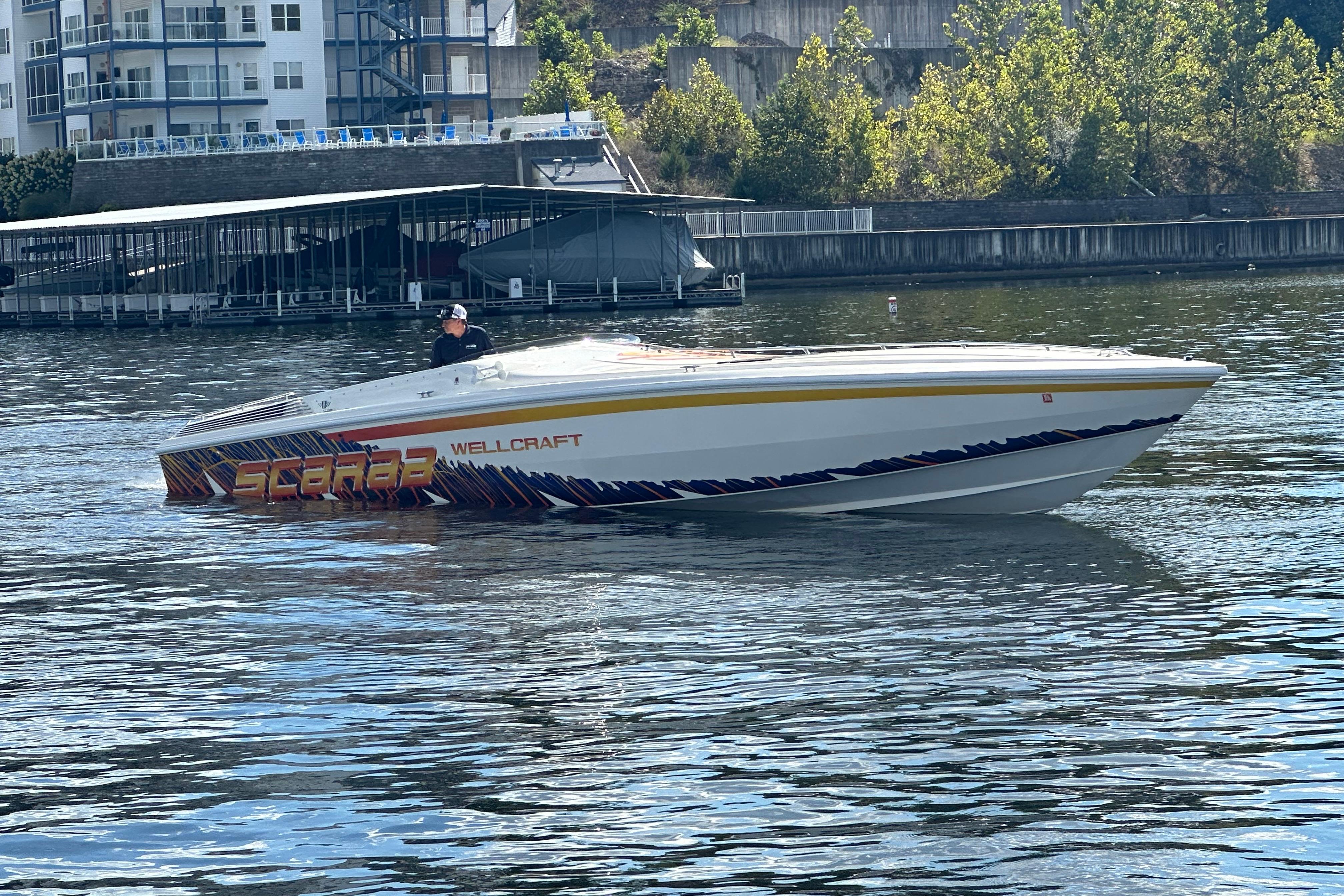 1995 Excel Scarab 43 speedboat on water near dock, vibrant graphics, sunny day.