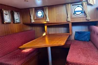 Cozy wooden boat interior with red cushioned seating, portholes, and nautical decor. Custom Belter 1240, 2002.