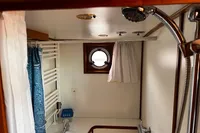 Compact bathroom with shower, porthole window, and blue curtain in 2002 Custom Belter 1240.