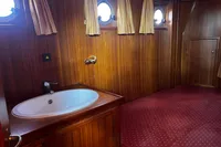 Wood-paneled bathroom with sink, porthole windows, and red carpet on a 2002 Custom Belter 1240.