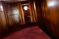 Wood-paneled cabin interior with porthole, curtains, and red carpet on a Custom Belter 1240, 2002.
