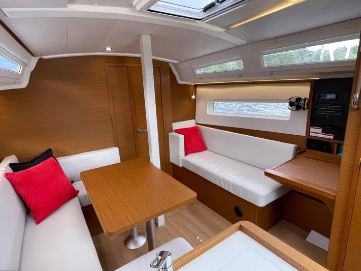  Yacht Photos Pics 2024 Jeanneau Sun Odyssey 380 interior with modern seating, wooden table, and red accent pillows.