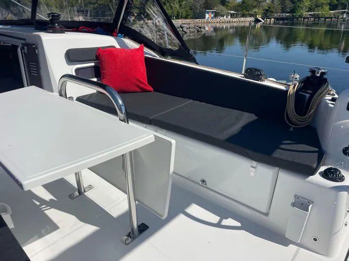  Yacht Photos Pics 2024 Jeanneau Sun Odyssey 380 cockpit with seating, table, and red cushion by the water.