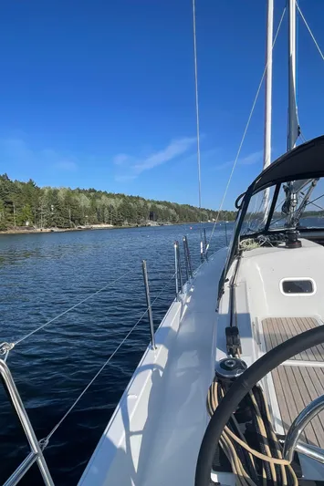  Yacht Photos Pics 2024 Jeanneau Sun Odyssey 380 sailing near a forested shoreline under clear blue skies.