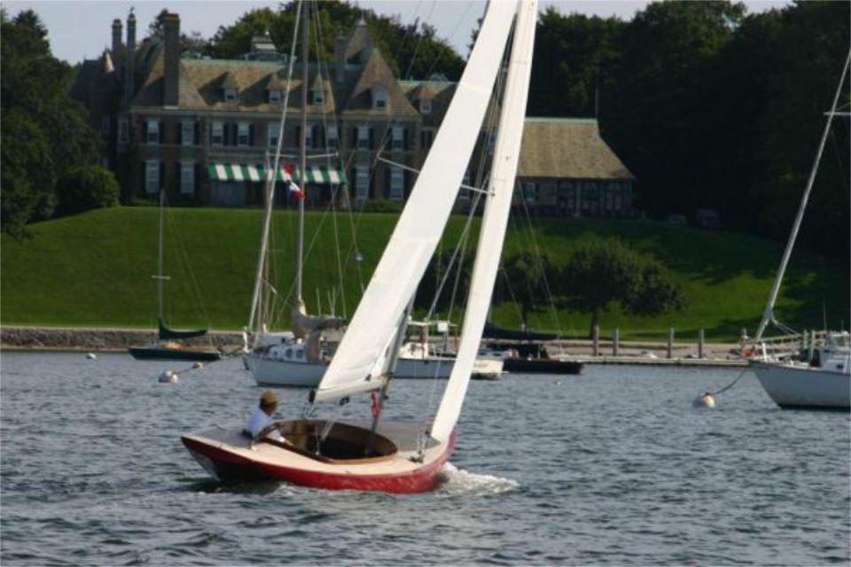 Sailboat Rustler 24 (2025) on water near elegant estate, lush greenery in background.