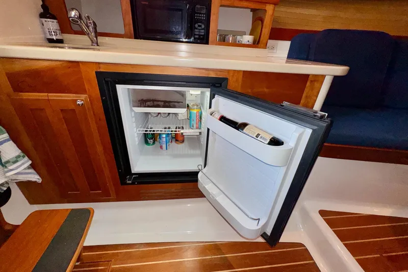 Tui Yacht Photos Pics 2005 Back Cove 29 boat interior with open mini fridge and wooden cabinetry.