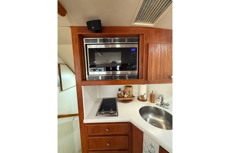  Yacht Photos Pics 1988 Bertram 43 Flybridge kitchen with microwave, stove, and sink in wooden cabinetry.